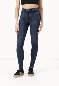 High-waisted blue denim jeans with a skinny fit, featuring subtle fading, five-pocket design, and stitched detailing along the seams.