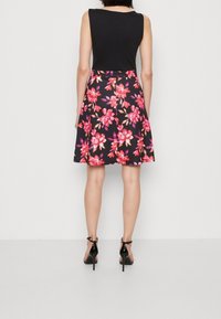 Haut sans manches noir avec une jupe évasée à motif floral, ornée de fleurs roses et violettes. Porté avec des sandales à talons hauts noires.