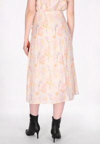 Blumiges Midikleid mit Pfirsich-, Gelb- und lila Mustern auf einem cremigen Hintergrund. Leichter Stoff, ausgestellter Saum, getragen mit schwarzen, hohen Stiefeln.