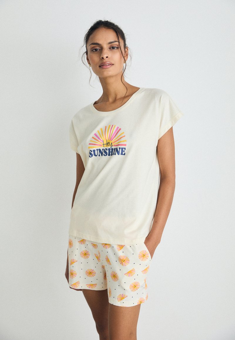 Cream short-sleeve t-shirt with "Hey Sunshine" print and sunburst design, paired with patterned shorts featuring colorful suns and black dots.