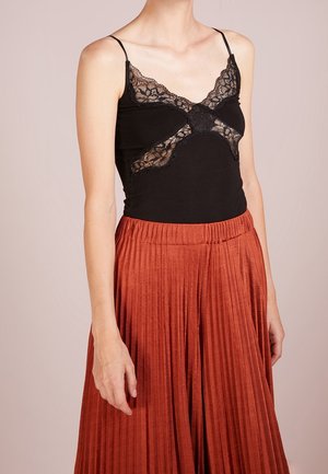 Mujer con top negro sin mangas con detalles de encaje y falda plisada color óxido de talle alto, vista desde el cuello hasta las caderas.