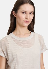 Jasno beżowy sweter z dzianiny z okrągłym dekoltem, krótkimi rękawami oraz siateczkową teksturą z delikatnym wzorem.