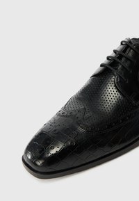 Černé kožené boty s perforovaným vzorem, se lesklým povrchem a texturovanými detaily v podobě krokodýlího vzoru na špičce.