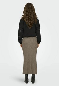 Sudadera negra con acentos bordados, combinada con una falda larga de canalé en taupe y botas negras de tobillo, vista desde atrás.