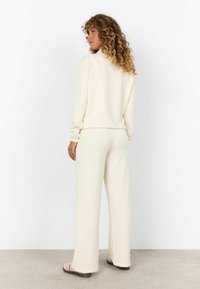 Kreemjatav loungewear komplekt sisaldab kõrge kaelusega särke ja laia säärega pükse. Kangas näeb välja pehme, minimaalsete detailidega ja puhaste joontega.