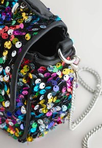 Svart väska täckt med flerfärgade paljetter och en texturerad yta. Har en silverkedjeslinga och svarta tygdetaljer.