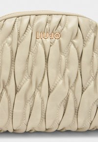 Beige gesteppte Tasche aus weichem Leder mit strukturierter Oberfläche und einem Roségoldenen "LIU·JO"-Logo. Mit Reißverschluss oben.