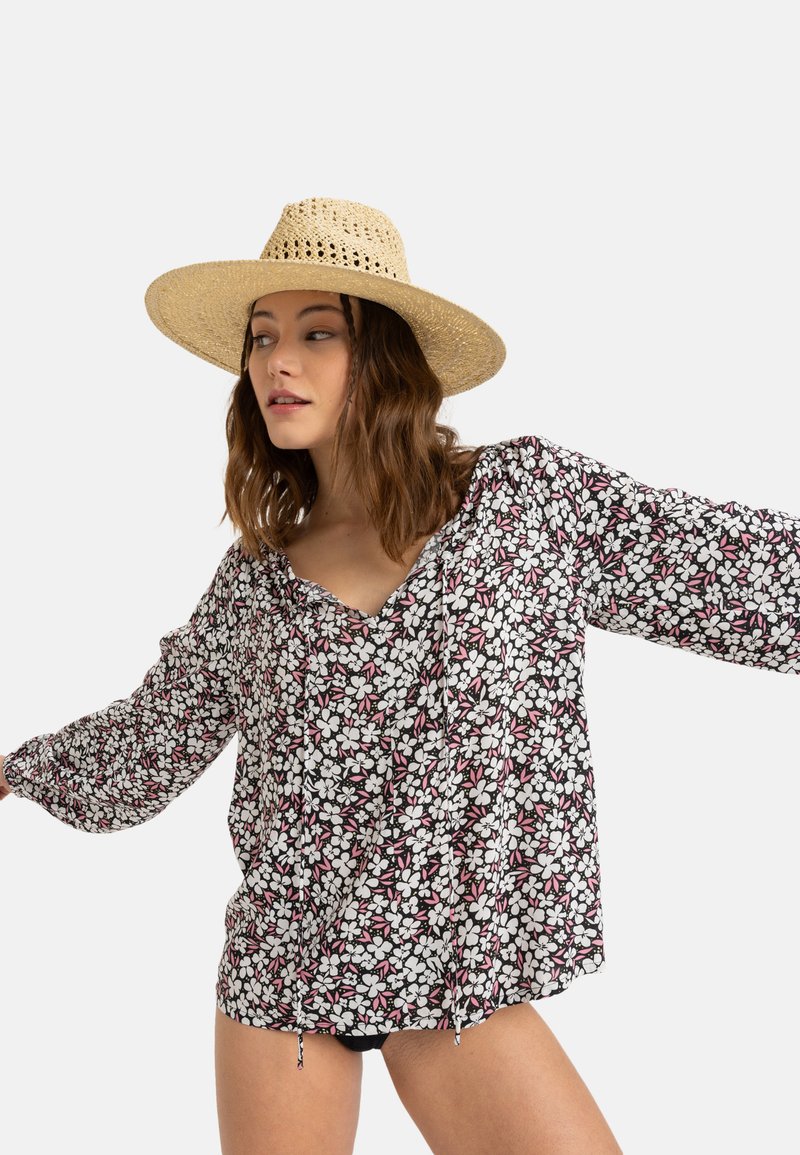 Černá květinová blůza s bílými a růžovými květy, dlouhé rukávy, výstřih do V a šňůrka na lemu. Nosená s kloboukem z trávy.