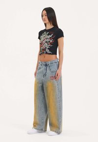 Black cropped t-shirt with graphic print; light blue wide-leg jeans with yellow gradient and red embroidery; white sneakers.
