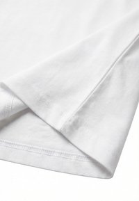 Gros plan sur l'ourlet et la couture de la manche d'un t-shirt blanc uni en coton montrant une couture fine et une texture de tissu douce.