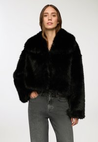 Czarna kurtka z sztucznego futra z krótkim krojem, szerokim kołnierzem i luźnymi rękawami. Połączona z szarymi dżinsami, które mają widoczne kieszenie i subtelną teksturę.