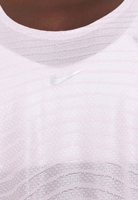 Lähikuva pinkistä Nike-urheilupaidasta, jossa on pieni valkoinen Nike-swoosh-logo hengittävässä verkkokudoksessa.