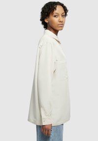 Camicia beige chiaro a maniche lunghe con colletto, taschino sul petto e polsini con bottoni, realizzata in un tessuto liscio.