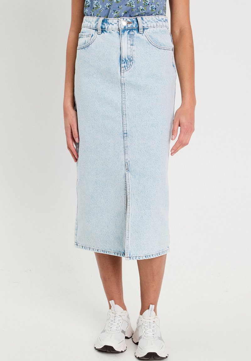 Helles blaues Denim-Midi-Rock mit einem Schlitz vorne, Fünf-Taschen-Design und Gürtelschlaufen. Kombiniert mit weißen Turnschuhen.