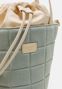 Jasnoniebieska pikowana torba typu bucket z denimu, z beżowym ściągaczem i beżowymi skórzanymi paskami, ozdobiona złotą plakietką z logo Joop! Jeans.