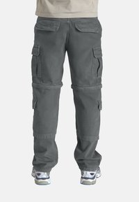 Pantalons cargo gris avec de multiples poches latérales et arrière, jambes fuselées et ourlets retroussés, confectionnés en tissu durable, associés à des chaussures de sport.