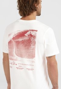 T-shirt bianca in cotone con un design grafico rosso che raffigura un surfista e un'onda, con testo che riporta O'Neill e le località dei negozi. Visto da dietro.
