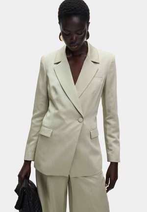 Blazer verde claro, entallado, con solapa con muesca, cierre de un solo botón y dos bolsillos delanteros. Textura suave, diseño minimalista.