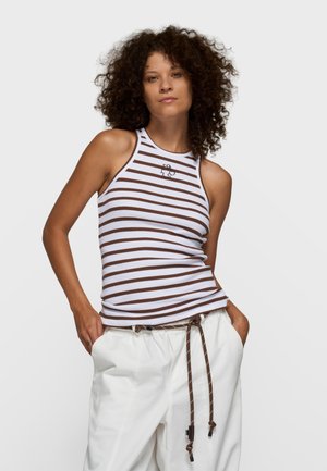 Biało-brązowy, bezrękawnik w paski z wysokim kołnierzem i haftowanym detalem. Noszony z jasnymi, luźnymi spodniami.