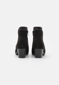Botas de tobillo de ante negro con punta redonda, tacón corto y apilado, y cierres laterales. Textura suave con un sutil detalle de costura en las costuras.