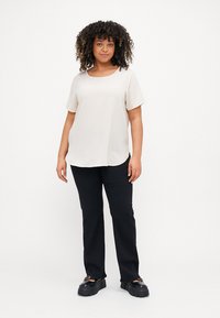 Light beige short-sleeve top with a rounded neckline, paired with black straight-leg pants and chunky black shoes. Simple, smooth texture.