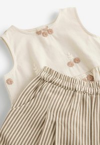 Sleeveless beige dress with brown and white floral embroidery on top and beige and white vertical striped skirt with elastic waist.