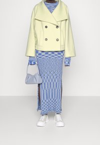 Světlezelený dvouřadý kabát, modré maxi šaty s potiskem a bočními rozparky, světle modrá kabelka a bílé tenisky.