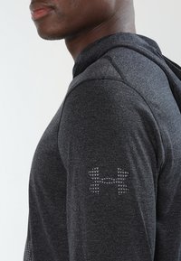 Szara bluza z kapturem z długim rękawem wykonana z teksturowanego materiału, z kapturem, dopasowanym krojem oraz logo w geometrycznym wzorze na rękawie.