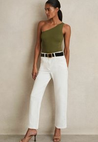 Body nero con spallina unica in verde oliva con dettagli in pizzo, abbinato a jeans bianchi a gamba dritta e una cintura nera con fibbia dorata. Sandali con tacco color cuoio.