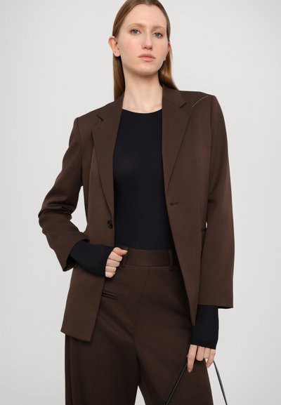 Brown tailored blazer with sharp lapels, single button closure, and slight shoulder padding, paired with a black fitted top and matching pants.