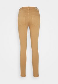 Vaqueros de mezclilla ajustados, en tono bronceado, con cintura alta, dos bolsillos traseros y dobladillos deshilachados. Textura suave, sin herrajes ni patrones visibles.