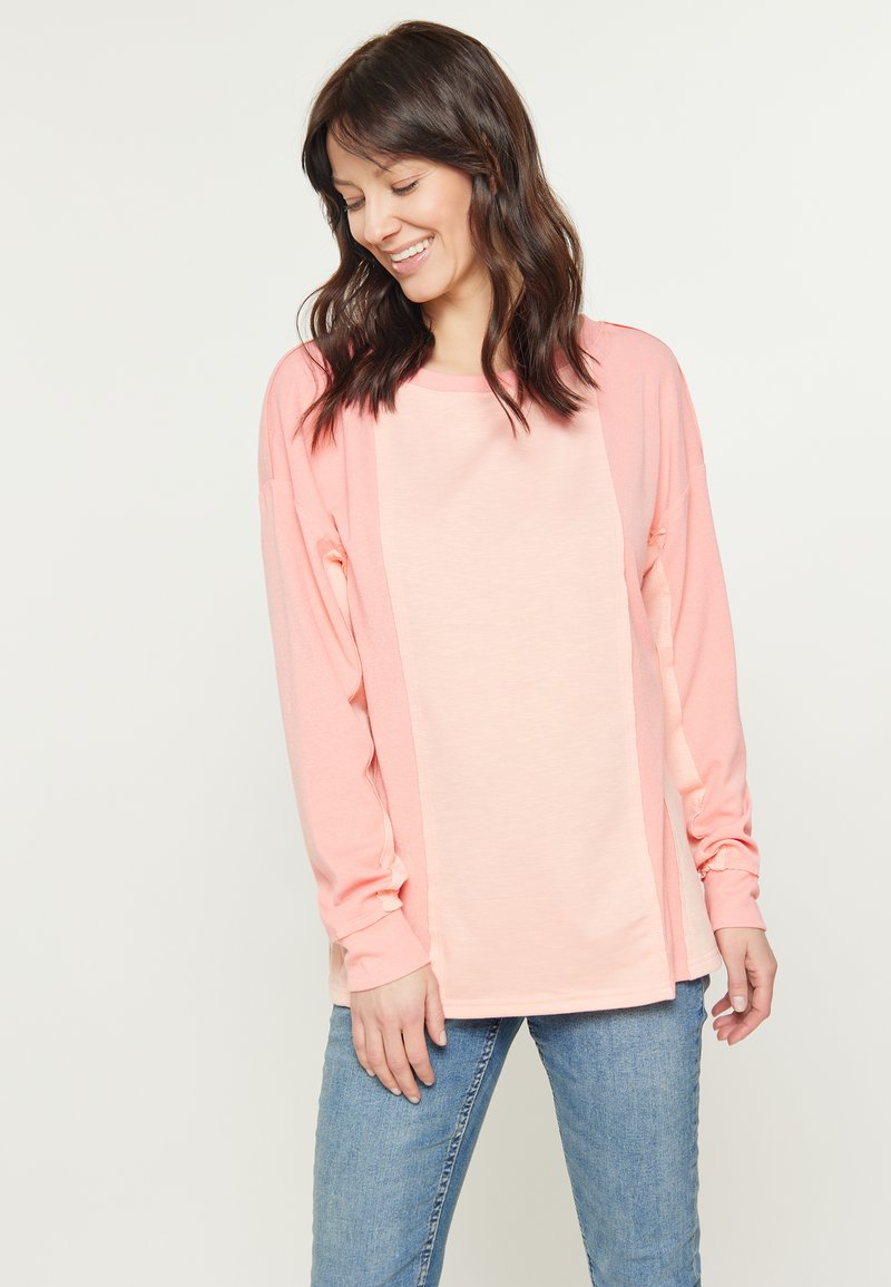Maglietta rosa chiaro a maniche lunghe con vestibilità comoda, scollatura rotonda e tessuto testurizzato con pannelli delle maniche contrastanti. Abbinata a jeans blu chiaro.