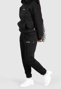 Svart huvtröja och mjukisshortser av mjukt tyg, med en framficka, ribbade ärmslut och vita logodetaljer. Tillsammans med vita sneakers.