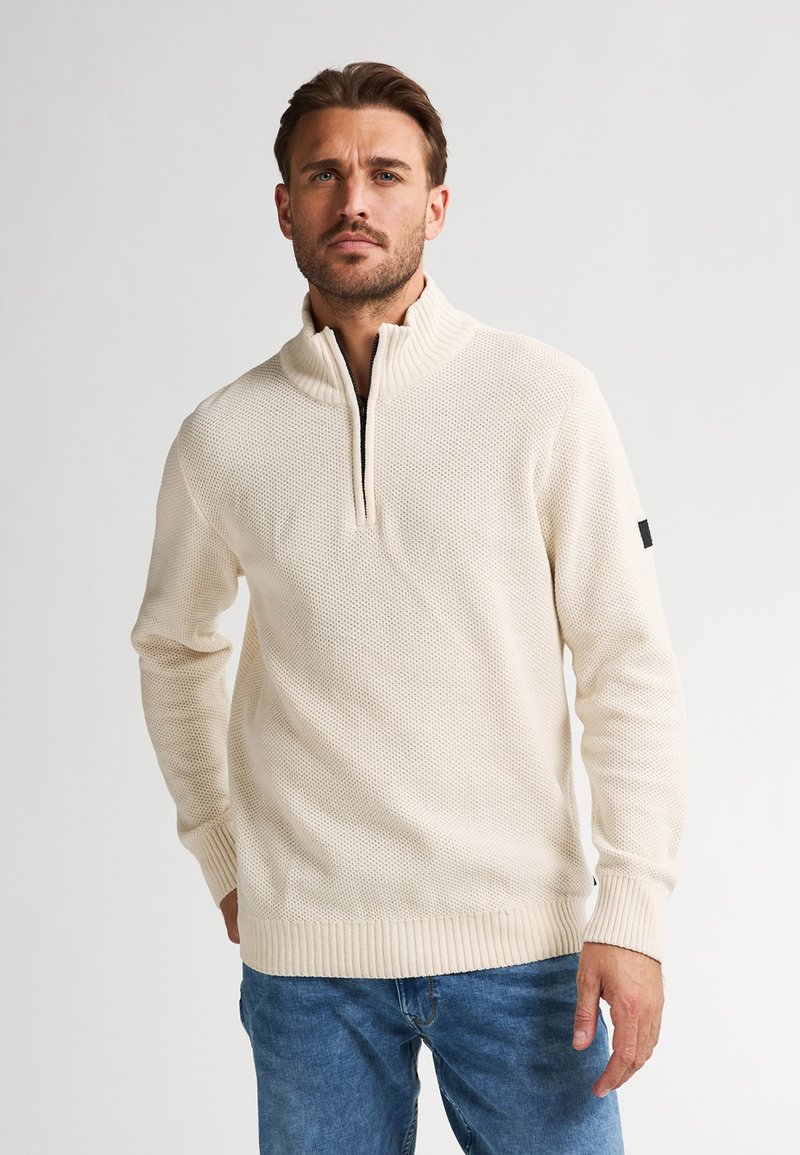 Maglione zip-up di colore beige chiaro con colletto alto, motivo a maglia testurizzato, polsini e orlo a coste. Piccolo dettaglio nero sulla manica.