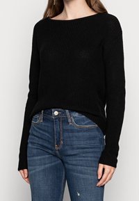 Maglione a coste nero con un ampio scollo e maniche lunghe, abbinato a jeans in denim blu con vestibilità classica e leggero scolorimento.
