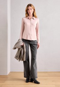 Lyse rosa langermet skjorte med knapper, grå svakt utsvingte jeans og en rutete blazer. Personen har på seg svarte ankelboots med hæl. Teksturerte og glatte materialer.
