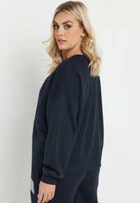 Felpa oversize blu navy con scollatura tonda e polsini a coste, caratterizzata da un motivo grafico testurizzato sul petto.