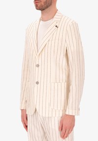 Blazer bianco con righe marroni, colletto a revers, due bottoni e tasche frontali. Tessuto morbido con finitura testurizzata.