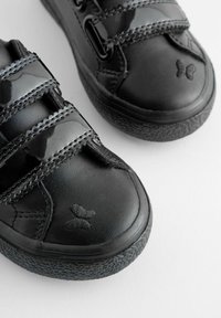 Czarne sneakersy z teksturowanymi gumowymi podeszwami, lakierowanymi paskami i wytłoczonym detalem motyla na palcu.