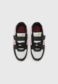 Baskets noires et blanches avec une sangle velcro, dotées d'une tige texturée, d'un bout perforé et d'accents rouges sur les côtés. Détail logo doré.
