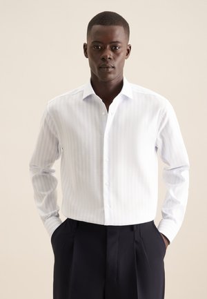 Chemise blanche à boutons avec des rayures verticales bleu clair, à manches longues et col classique. Associée à un pantalon sombre, avec des poches avant.