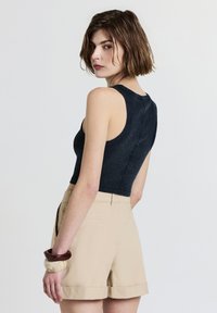Débardeur en denim foncé, cropped, avec un col rond associé à un short beige clair taillé, présentant une texture lisse et des poches latérales.
