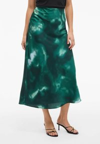 Jupe maxi en satin vert présentant un design fluide avec des motifs abstraits plus sombres, une texture lisse et un léger éclat, assortie de sandales à talons noires.