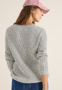 Pull en tricot gris clair avec un motif en relief, doté d'un col rond et de manches longues, associé à une casquette en velours côtelé rose.
