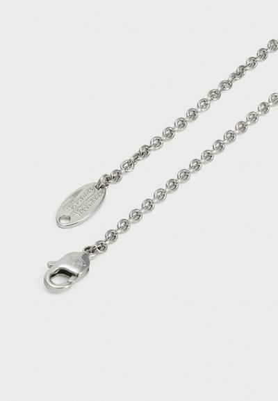 Collier chaîne en argent avec une plaque ovale gravée et un fermoir mousqueton, présenté en diagonale sur un fond clair uni.