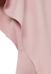 Tissu rose pâle avec un design drapé asymétrique en couches et des coutures fines le long des bords, créant une texture fluide et élégante.