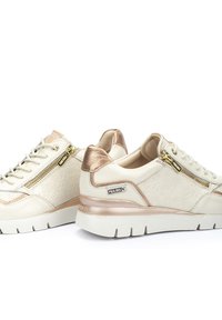 Baskets blanches avec des accents dorés, motif floral texturé sur les côtés, dotées d'une fermeture éclair sur le côté et d'une semelle épaisse blanche. Logo de la marque sur le talon.