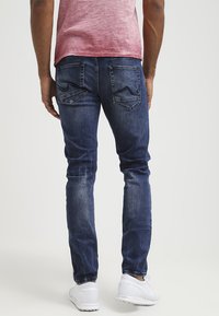 Jeans de denim azul ajustados con un lavado desgastado, costuras detalladas y bolsillos traseros con un patrón de chevron distintivo.
