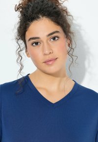 Tričko s výstřihem do V a krátkými rukávy v jednobarevné tmavě modré látce. Hladká textura s volnějším střihem, zdobené jemnými švy.
