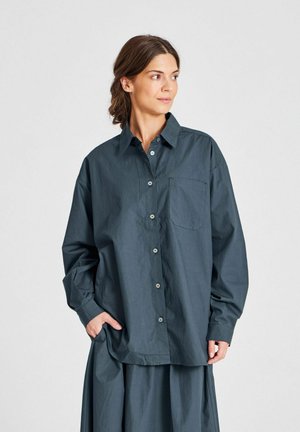 Camicia grigia scura con bottoni realizzata in tessuto leggero. Presenta un colletto a punta, maniche lunghe e una tasca sul petto. Texture liscia.